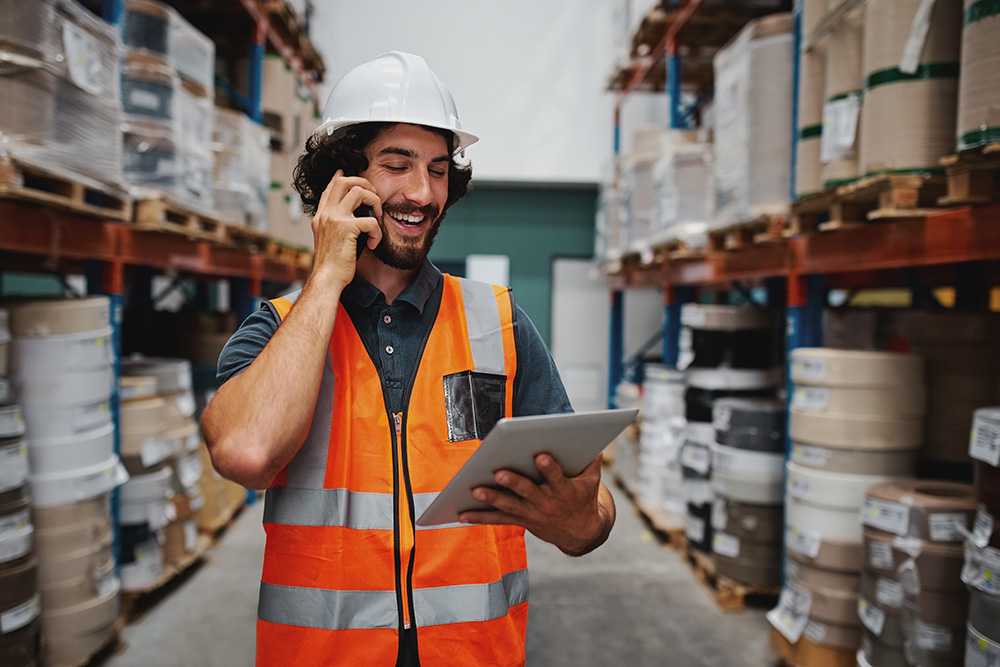 Worker in warehouse talking on the phone and looking at a tablet